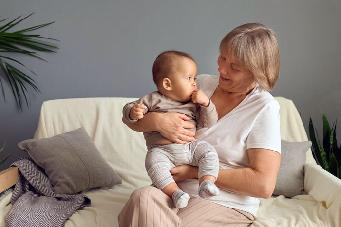 Elderly woman smiling while holding and kissing a newborn baby indoors on a cozy couch setting. Elderly woman smiling while holding and kissing a newborn baby indoors on a cozy couch setting.