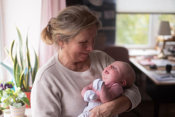 Woman lovingly holding and mil keeps kissing newborn in a cozy, softly lit home environment with plants in background Woman lovingly holding and mil keeps kissing newborn in a cozy, softly lit home environment with plants in background