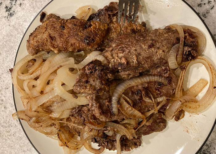 Plate of overcooked meat with onions, representing expired food in her pantry from 1999.