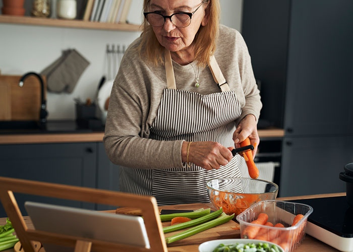 Older woman peeling carrots in a kitchen, illustrating expired food concerns and family meal disagreements. Older woman peeling carrots in a kitchen, illustrating expired food concerns and family meal disagreements.