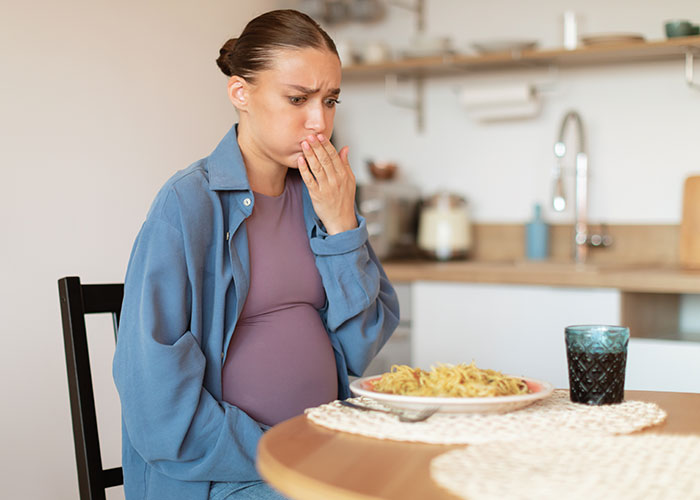 Pregnant woman looking upset at a plate of food in her kitchen, reacting to expired food in her pantry. Pregnant woman looking upset at a plate of food in her kitchen, reacting to expired food in her pantry.