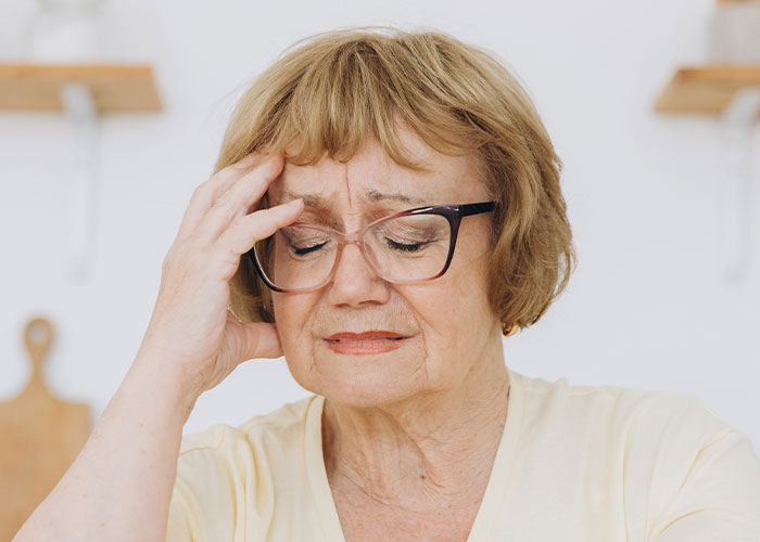 Older woman with glasses looks distressed while touching her forehead, related to expired food in her pantry from 1999.