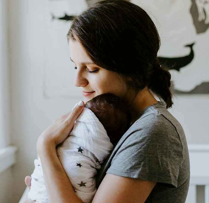 Mom takes her baby, cradling swaddled newborn against her chest in a calm nursery Mom takes her baby, cradling swaddled newborn against her chest in a calm nursery