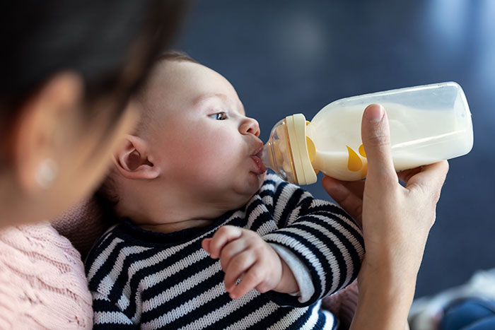 Mom takes her baby bottle-feeding an infant in a striped sweater held close Mom takes her baby bottle-feeding an infant in a striped sweater held close