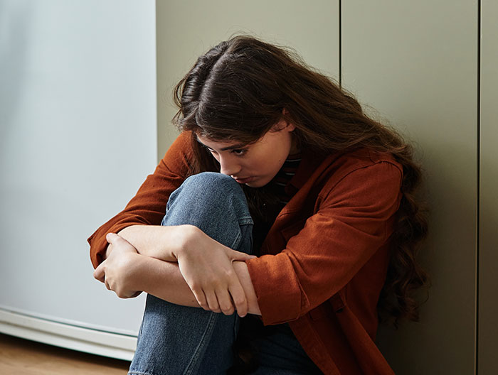 Sad woman hugging knees on floor, representing mom takes her baby and storms off after feeding dispute with MIL Sad woman hugging knees on floor, representing mom takes her baby and storms off after feeding dispute with MIL