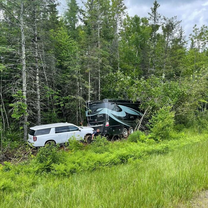White SUV stuck towing a large trailer in a forested area, illustrating an unfortunate and expensive fail.