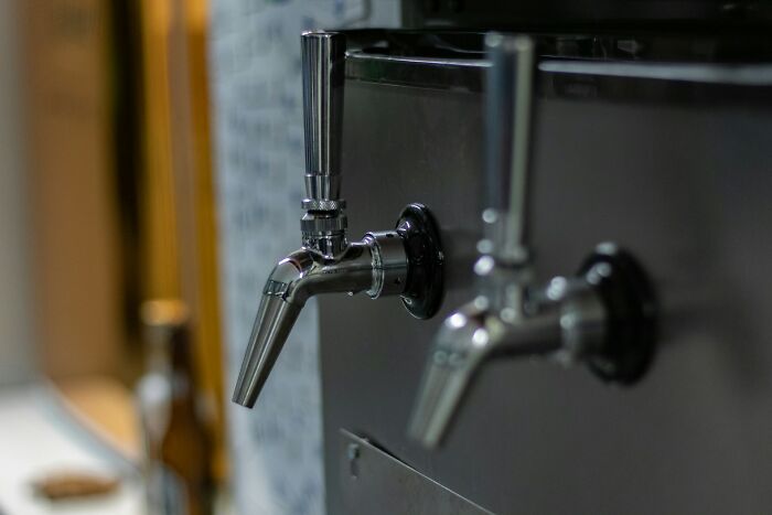 Close-up of a modern beer tap in a brewery showing people working in boring industries behind scenes.