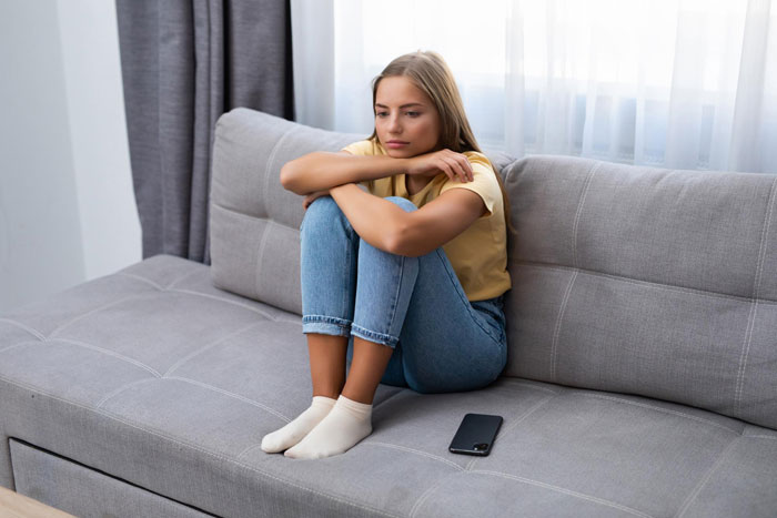 Young woman sitting on a couch looking upset, illustrating mom boyfriend food drama and emotional tension at home. Young woman sitting on a couch looking upset, illustrating mom boyfriend food drama and emotional tension at home.