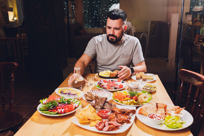 Man looking concerned with a large spread of food, representing mom boyfriend food drama at the dining table.