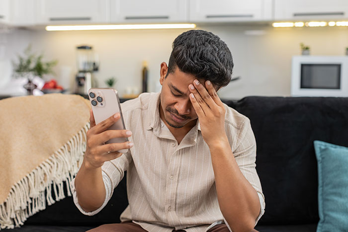 Adult son sitting on couch, holding phone with stressed expression, dealing with religious mom's guilt trips and biblical sermons. Adult son sitting on couch, holding phone with stressed expression, dealing with religious mom's guilt trips and biblical sermons.