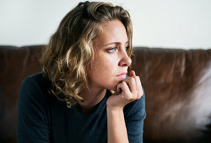 Pensive parent wonders about making daughter attend birthday, woman gazing thoughtfully on a couch Pensive parent wonders about making daughter attend birthday, woman gazing thoughtfully on a couch