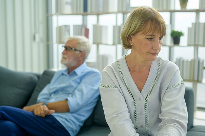 Selfish lady sits apart on sofa, woman looking away upset while man sits blurred behind