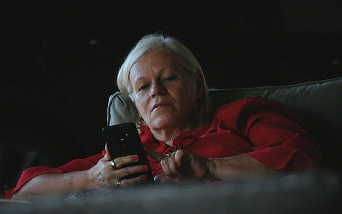 Selfish Lady keyword; older woman reclining on couch in red blouse, focused on her smartphone.