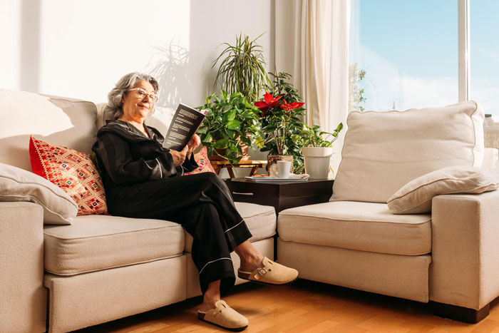 Older woman relaxing on a couch at home with plants nearby, reflecting on a mother airport trip drama story. Older woman relaxing on a couch at home with plants nearby, reflecting on a mother airport trip drama story.