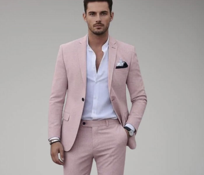 Groom wearing a stylish pink suit, standing confidently against a plain background, highlighting wedding attire choices.