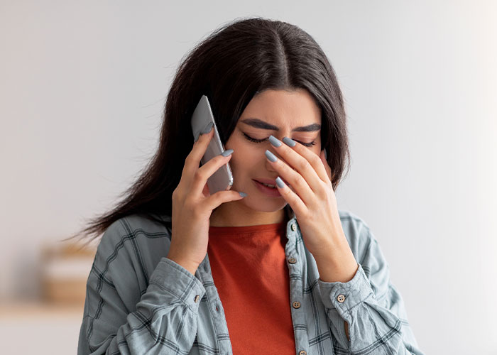 Young woman upset while on a phone call, reflecting emotional distress related to mom blaming daughter in divorce conflict. Young woman upset while on a phone call, reflecting emotional distress related to mom blaming daughter in divorce conflict.