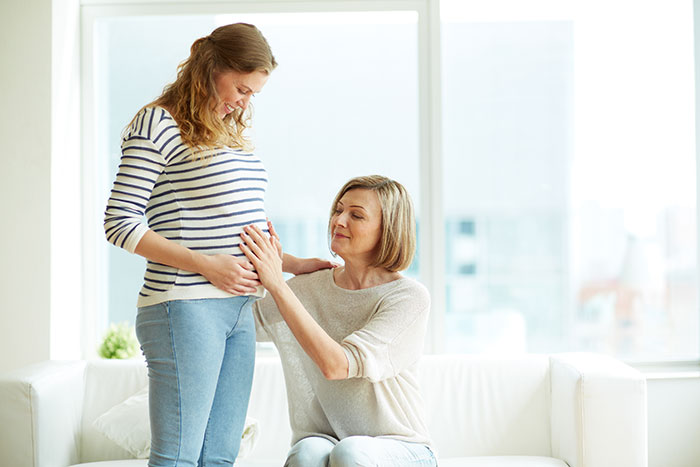 Pregnant woman standing while another woman sits touching her belly, highlighting family tension and no-contact after hospital incident. Pregnant woman standing while another woman sits touching her belly, highlighting family tension and no-contact after hospital incident.