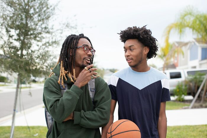 Two young men chatting outdoors, one holding a basketball, illustrating things normal in America but offensive elsewhere.