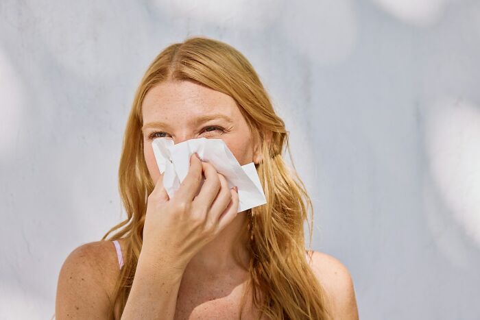 Young woman sneezing into tissue, illustrating things normal in America but offensive elsewhere in cultural behavior.