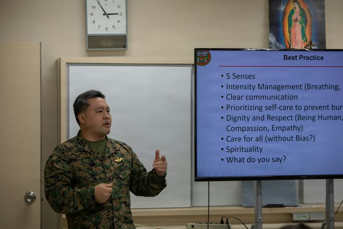 Man in camouflage giving a presentation on best practices, highlighting communication and respect in office rules context.