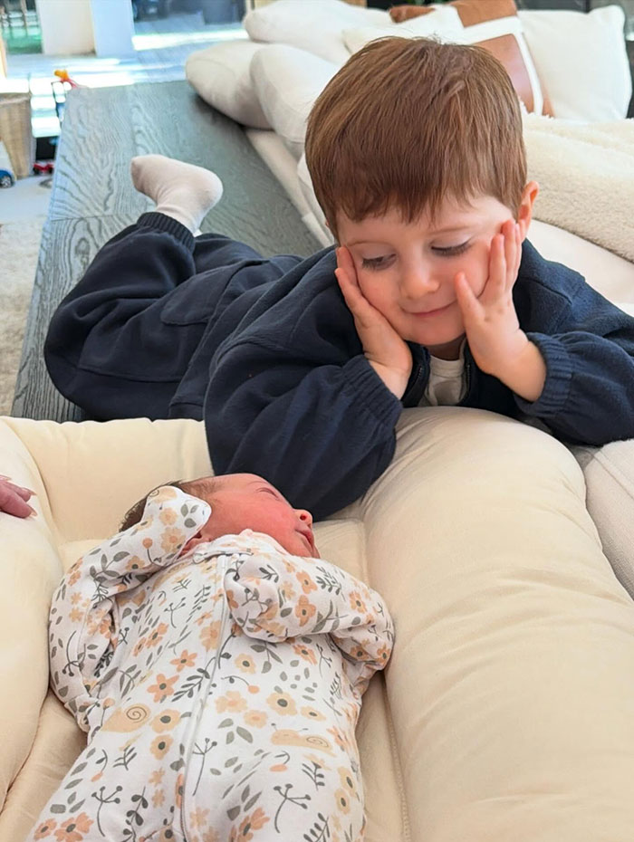 Young child lying next to newborn baby in floral outfit, capturing Meghan Trainor's secret surrogate baby moment performative scene. Young child lying next to newborn baby in floral outfit, capturing Meghan Trainor's secret surrogate baby moment performative scene.