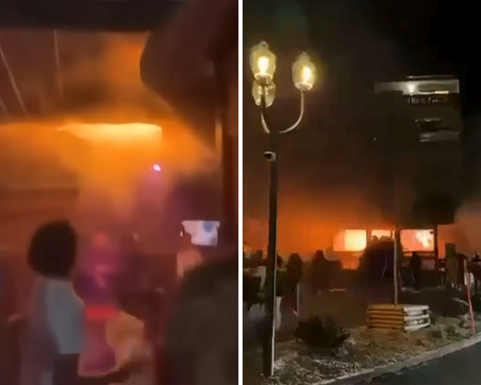 Orange flames and smoke engulf Swiss resort at night after horrific blaze, with people observing the scene from outside.