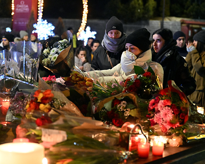 People wearing winter clothes lay flowers and light candles at a memorial for victims of the Swiss resort blaze tragedy.