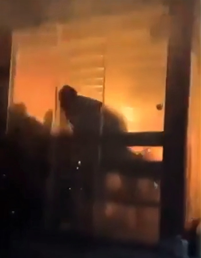 Silhouette of person near window with intense fire and smoke inside a building showing possible Swiss ski bar fire negligence.
