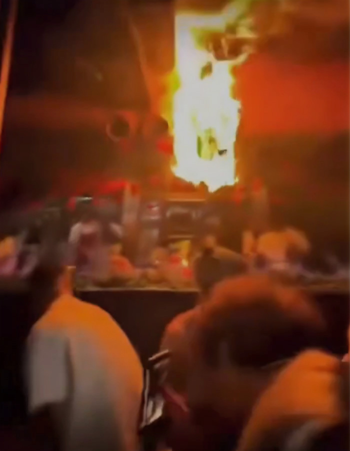 Fire blazing inside a Swiss ski bar with blurred patrons nearby, suggesting possible negligence causing the lethal incident. Fire blazing inside a Swiss ski bar with blurred patrons nearby, suggesting possible negligence causing the lethal incident.