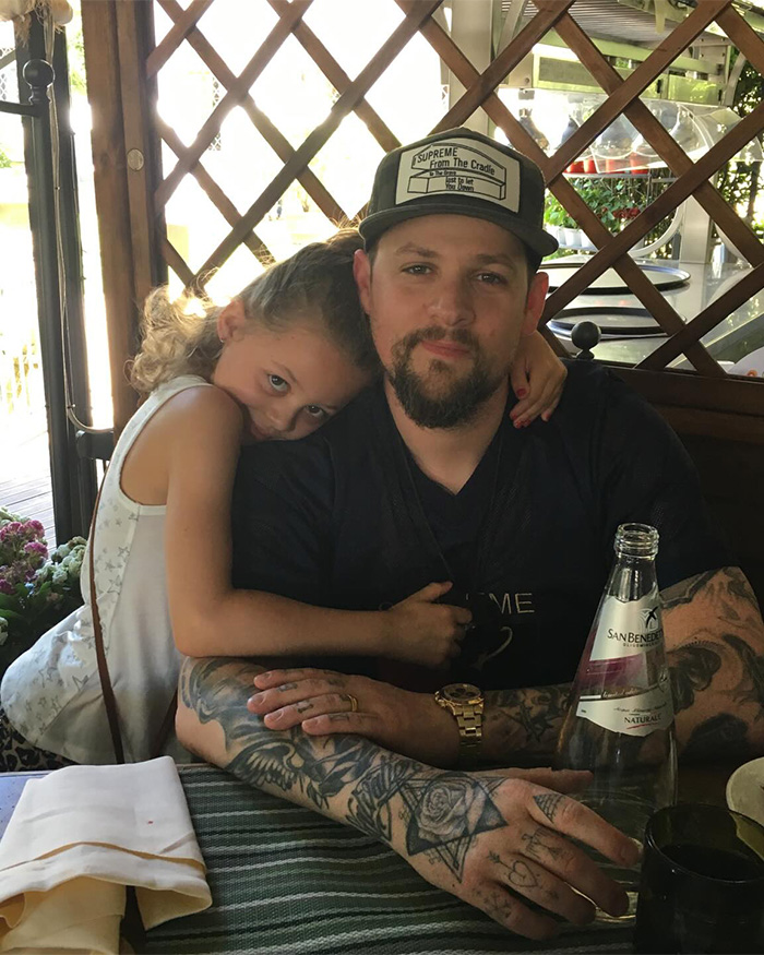 Man with tattoos and cap sitting at a table with young girl hugging him, related to Nicole Richie daughter new name news.