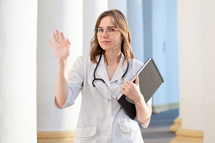 Female doctor with stethoscope raising hand, holding clipboard, representing newborns looking nothing like the father confusion.