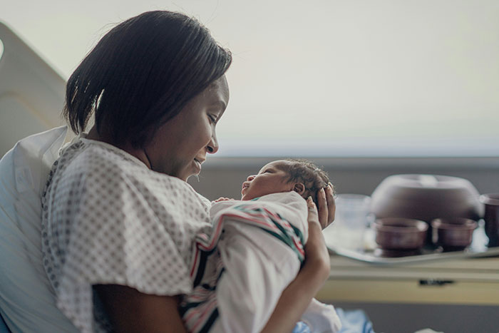 Mother holding her newborn baby in a hospital room, illustrating newborns looking nothing like the father causing confusion.