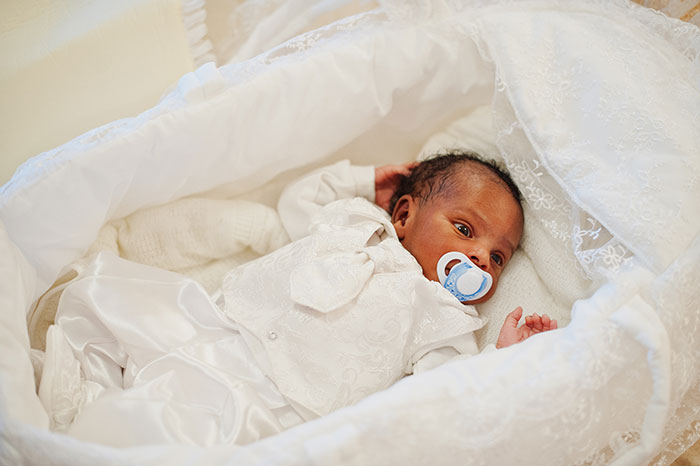 Newborn baby in white clothing lying in a bassinet, illustrating newborns looking nothing like the father.