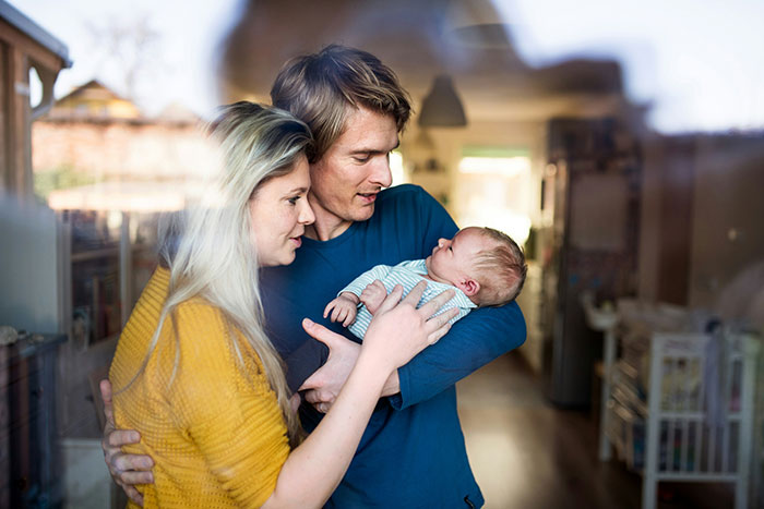 Young parents holding their newborn baby inside a cozy home, highlighting newborns that look nothing like the father.