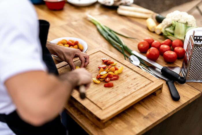 Person chopping colorful cherry tomatoes on a wooden cutting board preparing food in a kitchen setting
