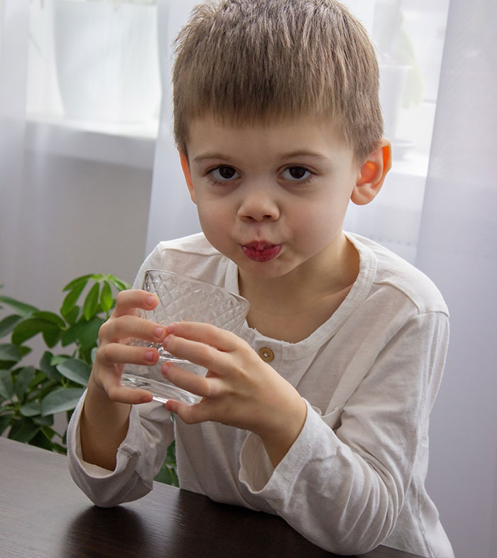 Young boy drinking water indoors, illustrating parenting differences around the world in child care and habits.