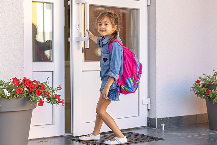 Young girl with a pink backpack entering a home, illustrating parenting differences around the world in various cultures.