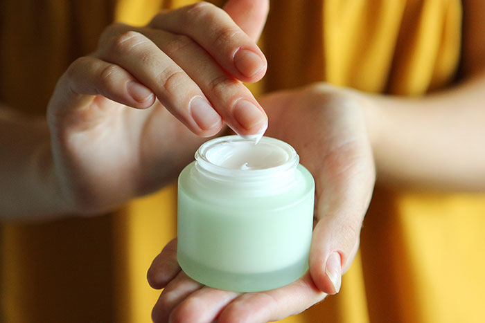 Person wearing yellow shirt using cream from a jar, illustrating parenting differences around the world concept.