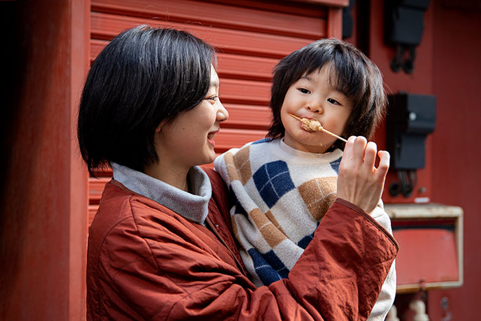 Mother feeding child a snack outdoors, illustrating parenting differences around the world with family bonding moments.