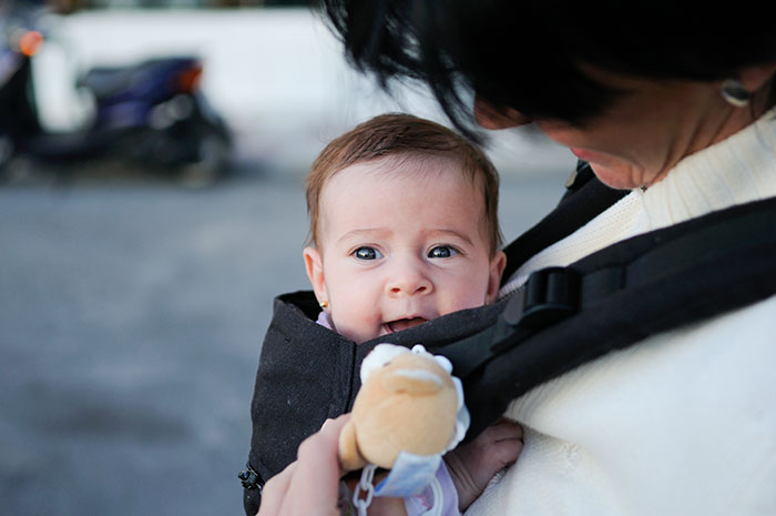 Baby in a carrier held by a parent outdoors, illustrating parenting differences around the world in childcare styles.