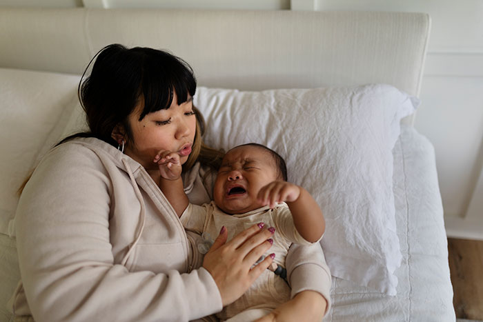 Mother soothing crying baby on bed, illustrating common parenting differences around the world in child care practices.