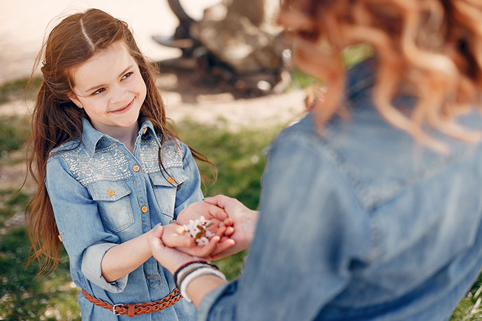 Young girl smiling at adult holding flowers in hands, illustrating parenting differences around the world concept.