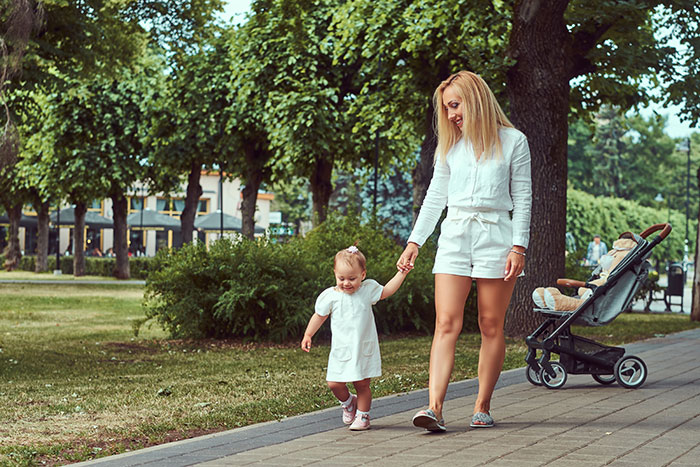 Mother and toddler walking hand in hand in a park, illustrating parenting differences around the world.