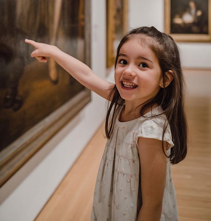 Young girl excitedly pointing at art in a gallery, illustrating different parenting styles around the world.