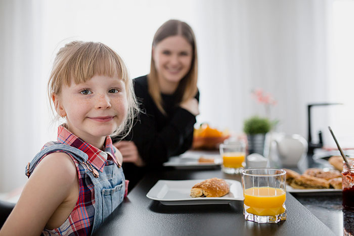 Smiling child and mother having breakfast together, illustrating parenting differences around the world at a modern dining table.