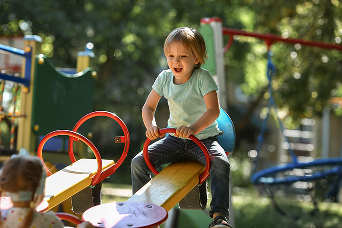 Child playing on a seesaw at a playground, illustrating parenting differences around the world in outdoor activities.