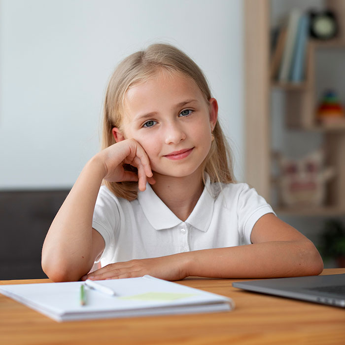 Young girl sitting at desk with notebook and laptop, representing parenting differences around the world in education settings.