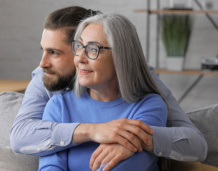 Older woman and younger man embracing on a couch, illustrating parenting differences around the world and family bonds.
