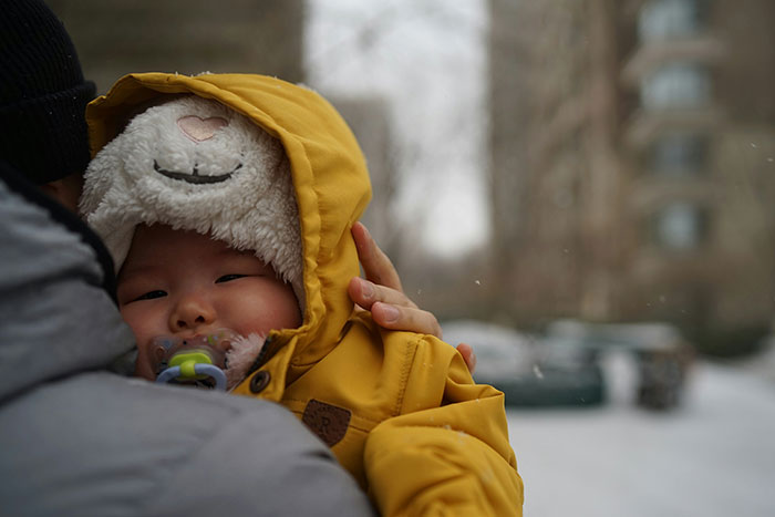 Baby bundled in a yellow jacket and pacifier held by a parent, illustrating parenting differences around the world in winter.