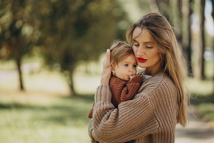 Mother in a cozy sweater holding her child outdoors, illustrating parenting differences around the world in a natural setting.